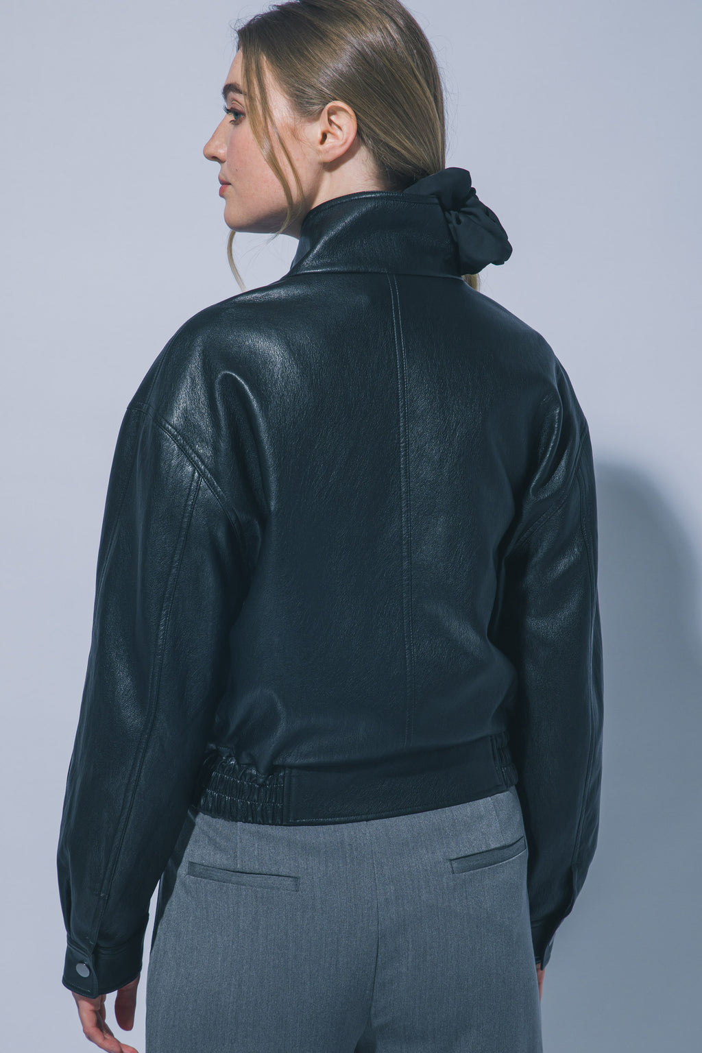 Women's cropped faux leather bomber jacket in Black – back view with elastic hem